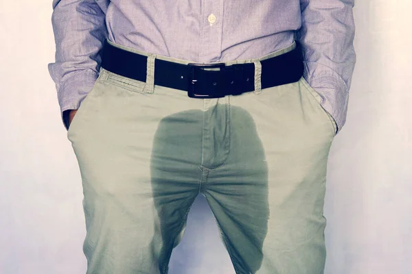 A man standing in wet pants against the wall. Urinary incontinence is an increasingly popular disease affecting younger males. incontinence and wet pants. a dark spot on a light trousers.