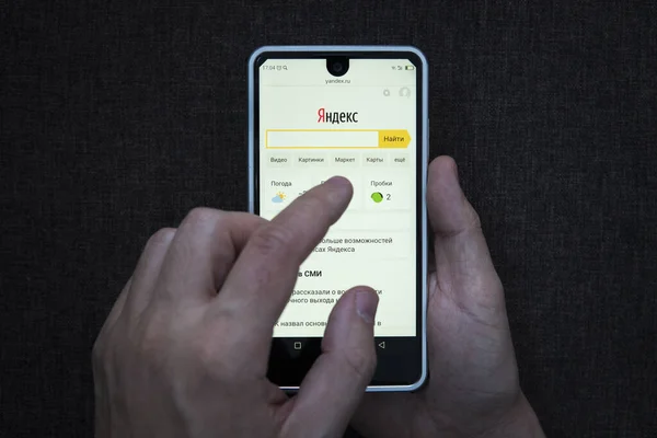 Hombre sosteniendo teléfono inteligente con el logotipo de Yandex con el dedo en la pantalla. Servicio de búsqueda ruso en smartphone . —  Fotos de Stock