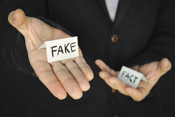 лист бумаги с поддельной надписью в руке мужчины на фоне другой руки с фактом надписи. Концепция обмана и манипуляции фактами
.