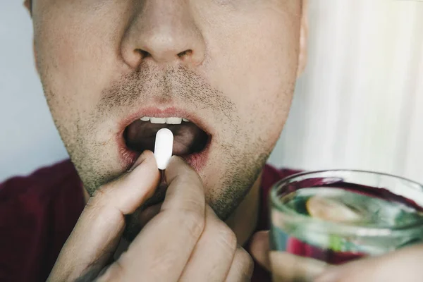 Homme avale la pilule et boit de l'eau. Jeune patient prenant une pilule et tenant un verre d'eau — Photo