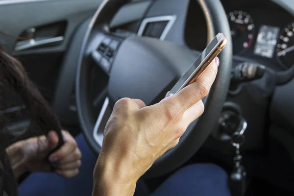 Primer plano de la mano femenina sosteniendo smatrphone y escribiendo mientras conduce. Mensaje de texto de la mujer usando el teléfono celular sentado en el coche. Respondiendo a la llamada mientras estaba al volante. Mano con teléfono en el fondo de la cabina del coche — Foto de Stock