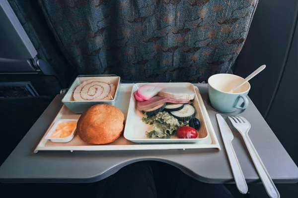 Comida Clase Turista. Aerolíneas. para comer en el avión. para alimentar a los pasajeros. conjunto de alimentos vista superior de cerca. salchicha con ensalada y pan y postre en un plato sobre la mesa plegable en plano — Foto de Stock