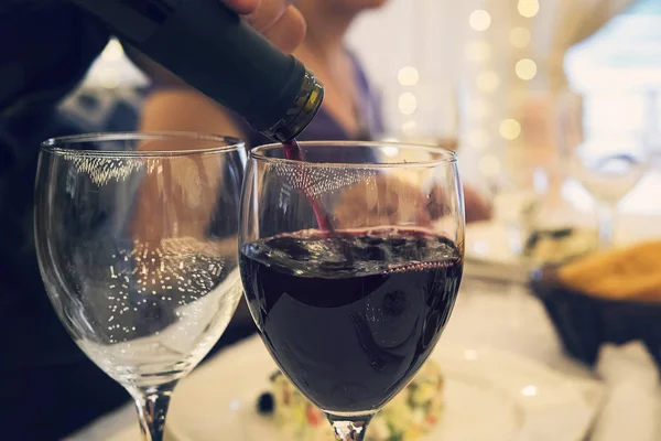 Zblízka dvě sklenice na stole restaurace s brýlemi na slavnostní večeři. Naplnění sklenice červeným vínem u slavnostního stolu. sommelier nalévá červené víno do sklenice. — Stock fotografie