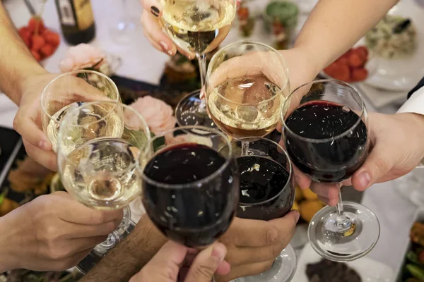 Friends clinking glasses above reataurant dinner table at some festive occasion. People drink toasts and clink tumblers at a formal dinner party. Drinking at a banquet. Men and women feast an event.