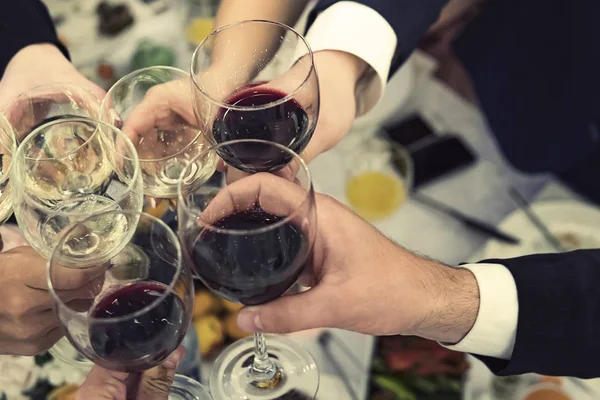 Pohled shora dolů z mužských a ženských rukou s vyplněnými sklenicemi vína nad jídelní stůl. Pití přípitky a cinkingů na večerní párty. Pití vína na banketu. Hostovat událost. — Stock fotografie