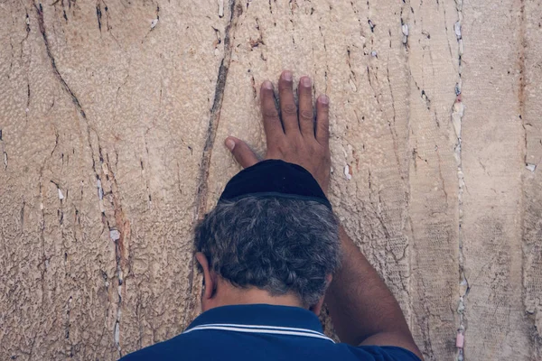 Еврейский ортодоксальный человек молится с сильными эмоциями у камней Западной Стены, одной из главных древних еврейских реликвий. Затылок старика, который касается известняковой стены и молится — стоковое фото