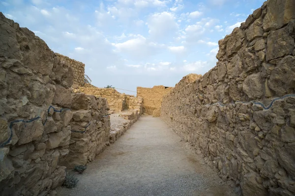 Panorama van een pad tussen niet hoge oude stenen muren tegen de blauwe bewolkte lucht. Lege weg tussen de muren van een oude Midden-Oosterse stad. Archeologie en opgraving bevindingen. Israël, Masada. — Stockfoto