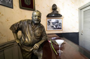 Glass of Daiquiri cocktail and statue of American writer Ernest Hemingway in the bar El Floridita in Havanna clipart
