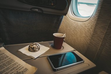 Uçuş sırasında eğlence. Uçuş sırasında monoton bir eğlence. Kahve, zencefilli çörek, bir kitap ve bir akıllı telefon katlama masasında arka planda uçak kanadı olan bir pencereye karşı..