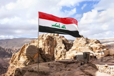 Flag of Islamic republic of Iraq waving in mountain background, cloudy skies