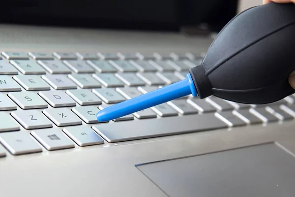 Gros plan de la main féminine balayant la poussière du clavier de l'ordinateur portable à l'aide d'une ampoule d'air — Photo