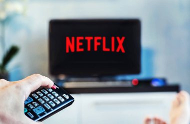 Genç bir adam evinde ve televizyonunda Netflix izliyor. Önplanda TV kumandası, TV 'de bulanık arkaplan.