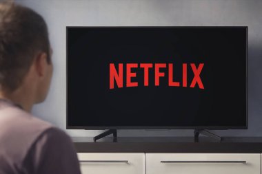Genç bir adam evinde ve televizyonunda Netflix izliyor. Önplanda TV kumandası, TV 'de bulanık arkaplan.