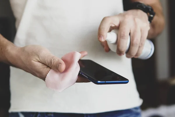 Hombre salpica en el teléfono inteligente un desinfectante para desinfectar y prevenir las enfermedades virales. Agente antimicrobiano antibacteriano para matar microbios. Agente limpiador para la limpieza . — Foto de Stock