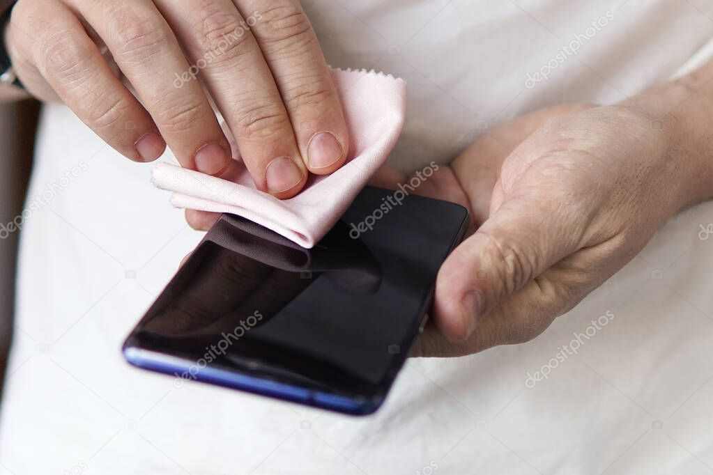 man rubs the screen of his black smartphone with a rag. Prevention of coronavirus and viral diseases. Cleaning the mobile phone from dust.