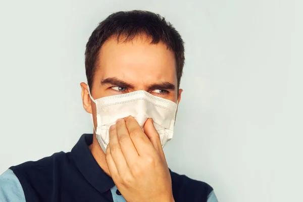 Portrait of a Male wears blue medical face mask. blue background. Fear of the coronavirus. unpleasant smell. Sour face. disgusting stench