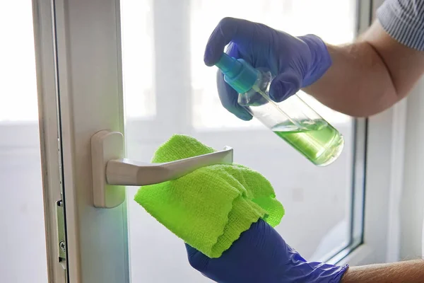 man disinfects door handle with disinfectant liquid. spraying door handle and wiping with a cloth. Disinfection of premises.prevention coronavirus, infectious diseases. Tidying up. window washing.