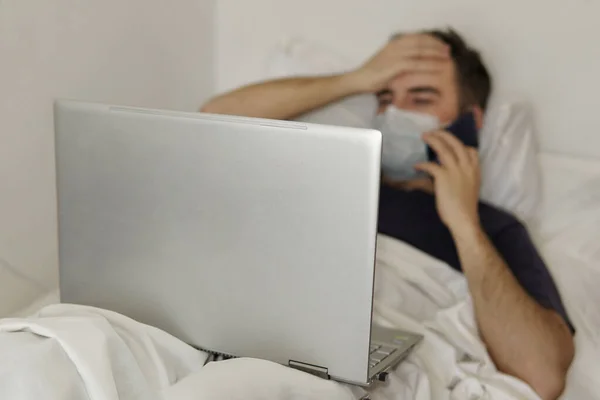 Um adulto está deitado na cama do hospital com um portátil a segurar a cabeça. Conceito de trabalho remoto durante a pandemia do coronavírus — Fotografia de Stock