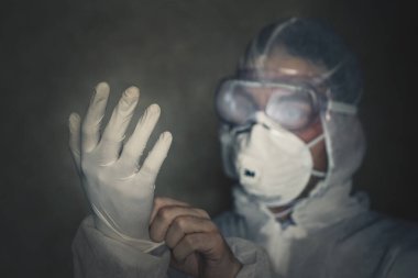 Adam koruyucu antiviral giysi giyer. Yakından eldiven takıyor. Karanlık odada. Gece çalış. Epidemiyolojik koruma giysisi içinde bir doktor..