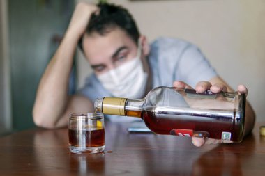 Alkolizm, alkol bağımlılığı ve evde rom şişesi olan erkek alkolik kavramı. Sıkıntıdan tek başına sarhoş olan işsiz bir uzman kendini izole ederek karantinaya alındı..