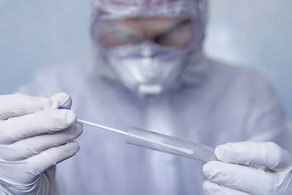 Hands in medical gloves holding empty plastic tube with blue cap for collection of analysis. a man in a chemical protection suit holds a test tube for analysis.