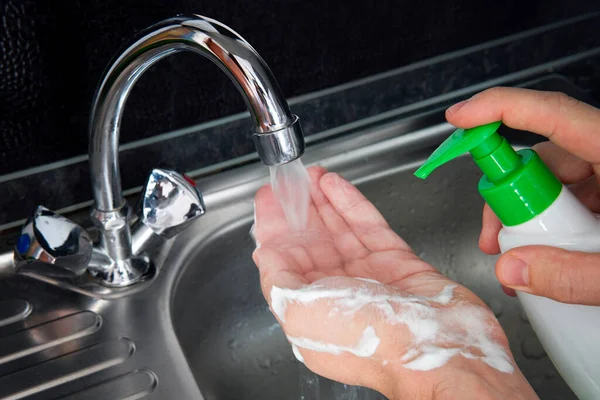 Wash your hands. a young guy washes his hands with soap under the faucet over a metal sink on a black dark background. Virus prevention. Hygienic procedure. liquid soap in a bottle.