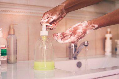 Suyun altında sabunla ellerini yıkamak. Afro-Amerikalı bir kadın ellerini yıkıyor. Sabun ve suyla şişeye bastır..