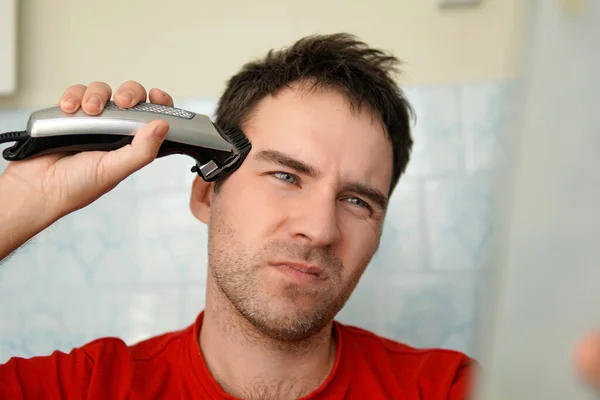A man cuts his hair on his head with an electric razor. Clean yourself up on your own. suffering from cutting hair