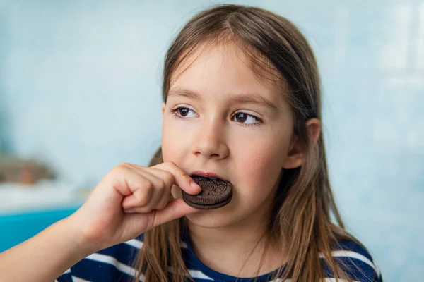 Närbild av en flicka som äter en rund chokladkaka sitter i köket hemma. Skadlig men utsökt mat. Sötma. — Stockfoto