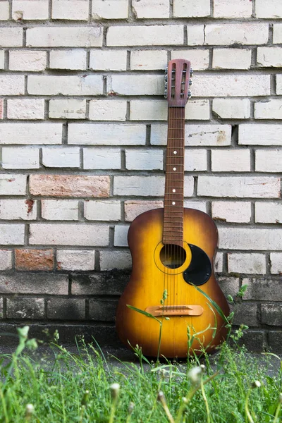 Guitarra acústica apoyada sobre una pared de ladrillo blanco — Foto de Stock