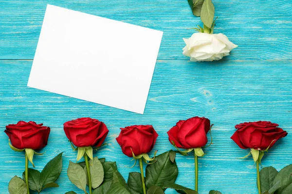 Rote und weiße Rosen mit leerer Papierkarte auf türkisfarbenem Tisch Stockfoto