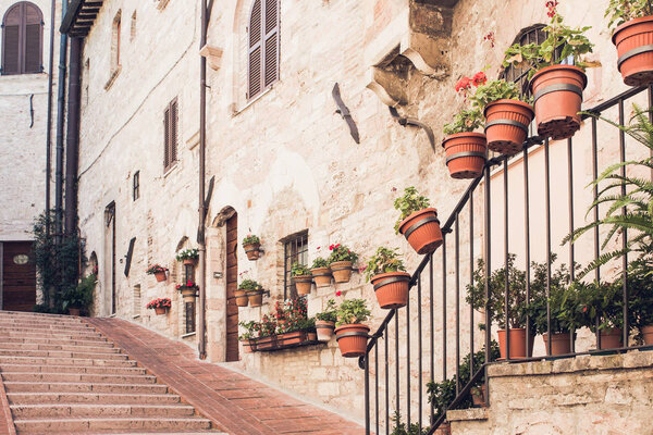 Narrow staircase street of the old town of Assisi with ancient stone houses decorated with flowerpots, Italy