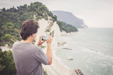 Genç adam alarak fotoğraf cep telefonunu üzerinde deniz manzara