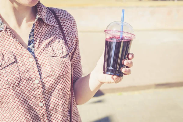 Woman holding berry drink in plastic cup with straw