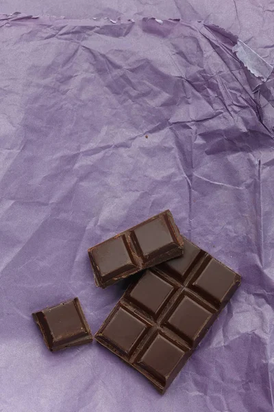 Barra de chocolate negro sobre papel morado arrugado —  Fotos de Stock