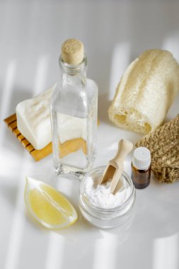 DIY ev temizliği için çevre dostu aletler ve malzemeler. Beyaz sirke, kabartma tozu ve limon, katı doğal sabun, aroma yağı ve beyaz masada luffa süngeri.
