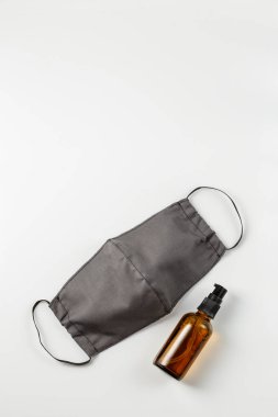 Beyaz arka planda yeniden kullanılabilir koruyucu pamuk maskesi ve cam bir şişe el dezenfektanı. Antibakteriyel hijyen yoluyla koronavirüs önleme