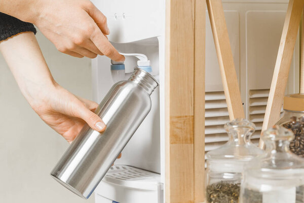 Женщина наливает воду в свою личную бутылку из нержавеющей стали. Концепция здоровых ежедневных привычек
