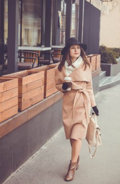 Bir fincan kahve ile şehir içinde genç kadın yürüyor
