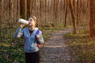 Kız uzun yürüyüşe çıkan kimse sırt çantası ile ormanda suyu içer