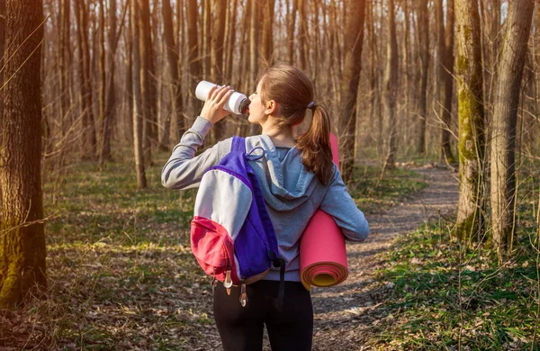 Girl hiker with backpack drinks water in the forest