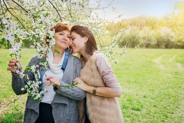 Madre de mediana edad y su hija abrazándose en el jardín floreciente —  Fotos de Stock