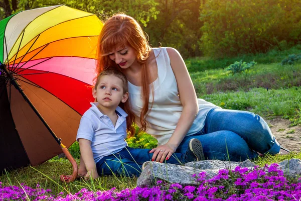 Młoda matka siedzi z jej synka w ogrodzie. Koncepcja dzień matki — Zdjęcie stockowe