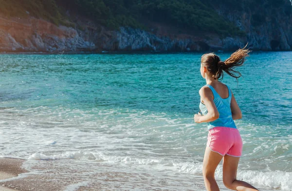 Genç bir kadın sahilde koşuyor.