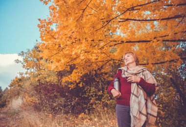 Orta yaşlı bir kadın içki çay sonbahar ormandaki
