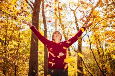Orta yaşlı kadın ormanda yaprakları atma