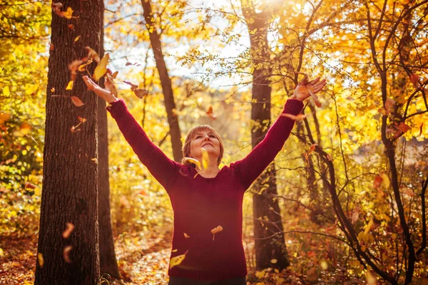 Middle-aged woman throwing leaves in the forest — Stock Photo, Image