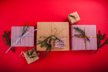 Çam dalları üzerinde kırmızı arka plan ile dekore edilmiş hediye kutuları.