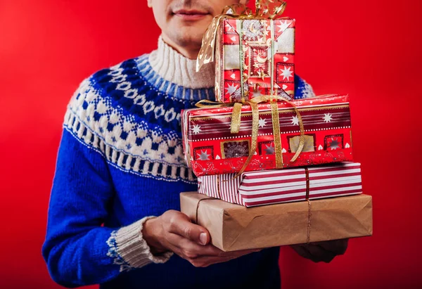 Estúdio de um jovem em suéter islandês segurando um monte de caixas de presente. Conceito de celebração de Natal ou Ano Novo . — Fotografia de Stock