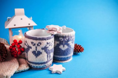 Mavi zemin üzerine örme Noel durumlarda sıcak içecek su bardağı giyinmiş.